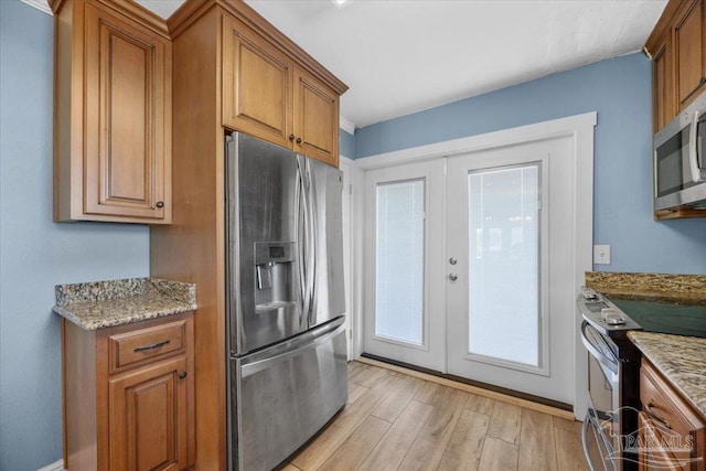 kitchen with light stone countertops, light hardwood / wood-style flooring, french doors, and appliances with stainless steel finishes