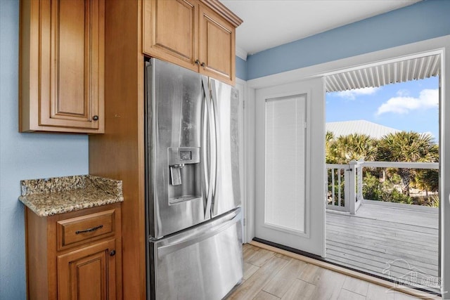 kitchen featuring light stone counters, light hardwood / wood-style floors, and stainless steel refrigerator with ice dispenser