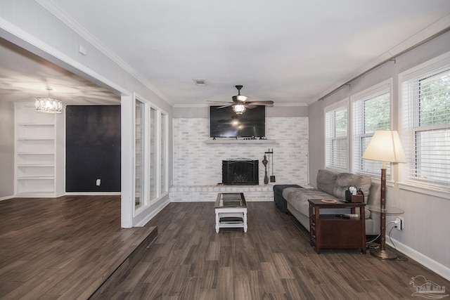 living room with dark wood-style flooring, crown molding, visible vents, a brick fireplace, and ceiling fan with notable chandelier