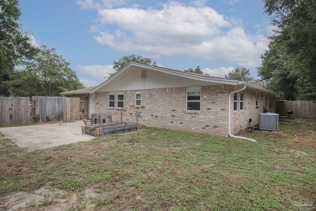 rear view of house with a fenced backyard, a yard, central air condition unit, a patio area, and brick siding