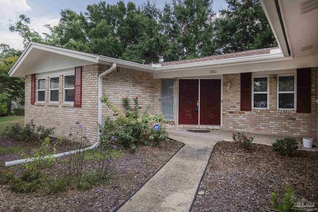 doorway to property featuring covered porch and brick siding