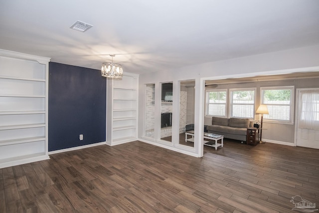 unfurnished living room with a notable chandelier, visible vents, built in features, baseboards, and dark wood finished floors