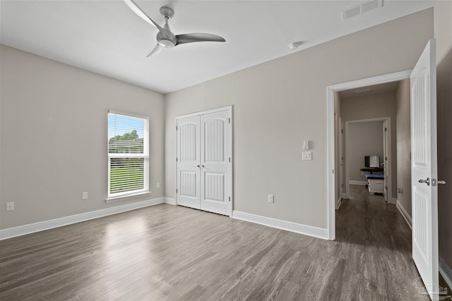 unfurnished bedroom with a closet, visible vents, wood finished floors, and baseboards