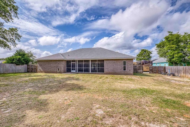 back of property featuring a sunroom, a lawn, a fenced backyard, and brick siding