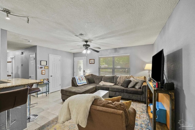 living room with a textured ceiling, ceiling fan, visible vents, and light tile patterned floors