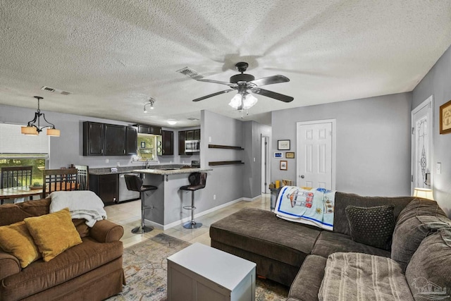 living area featuring light tile patterned floors, ceiling fan, a textured ceiling, and visible vents