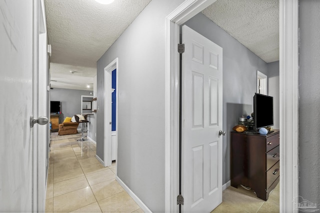 corridor featuring baseboards, a textured ceiling, and light tile patterned flooring