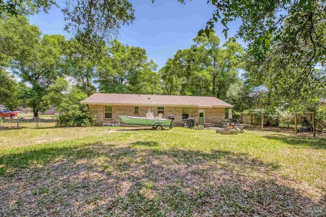 rear view of house featuring a yard, brick siding, fence, and an outdoor fire pit