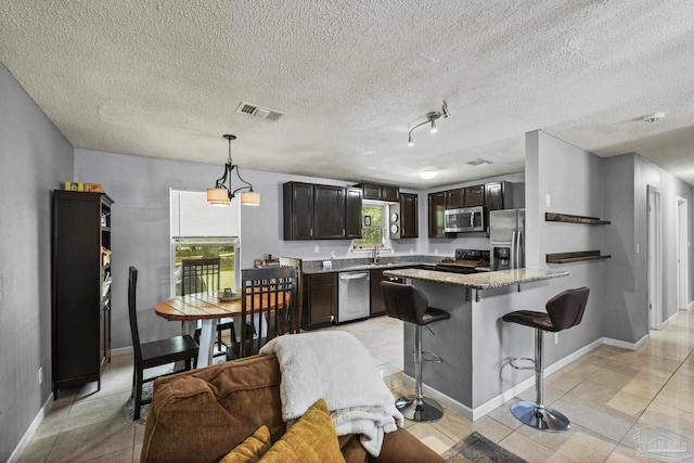 kitchen featuring visible vents, a peninsula, dark brown cabinetry, a kitchen bar, and stainless steel appliances