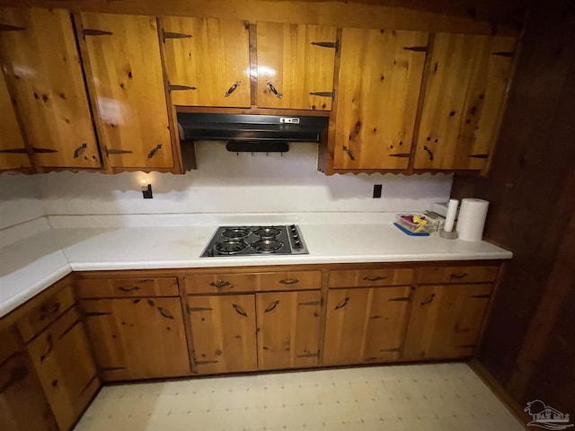 kitchen with under cabinet range hood, light floors, light countertops, brown cabinets, and gas stovetop