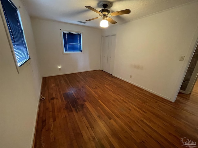 unfurnished bedroom featuring wood finished floors, visible vents, baseboards, ceiling fan, and a closet