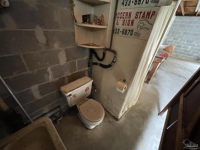 bathroom featuring unfinished concrete flooring, toilet, and concrete block wall