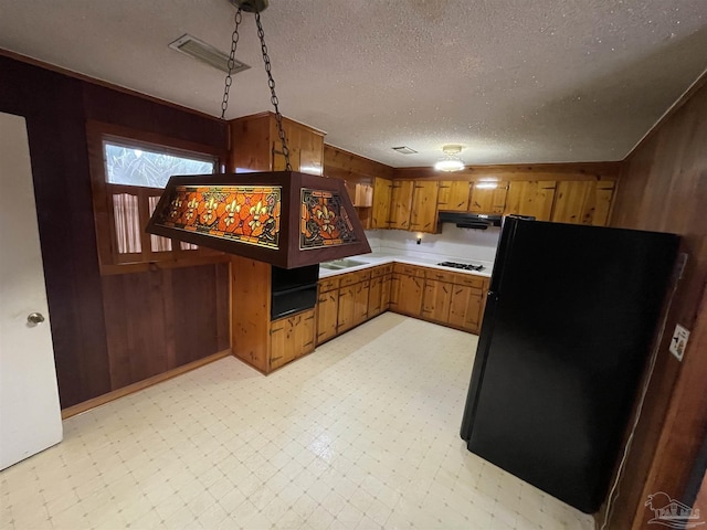 kitchen with wooden walls, light floors, brown cabinets, freestanding refrigerator, and gas stovetop