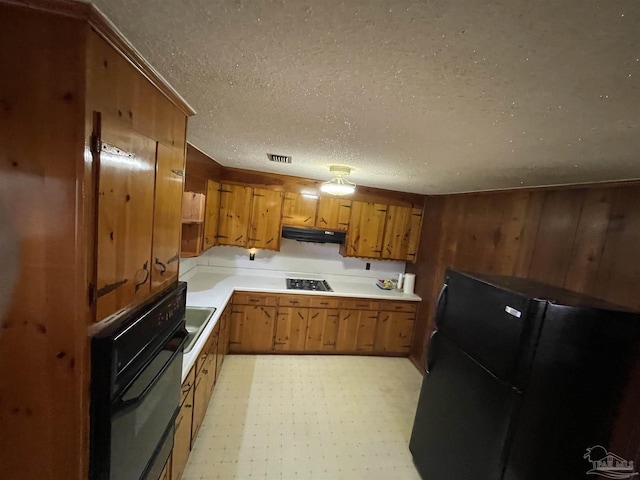 kitchen featuring visible vents, gas stovetop, freestanding refrigerator, under cabinet range hood, and brown cabinets