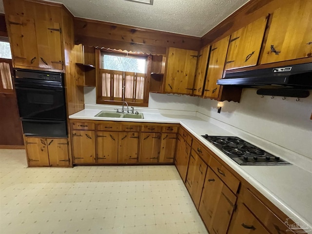 kitchen featuring under cabinet range hood, light floors, black appliances, a warming drawer, and a sink