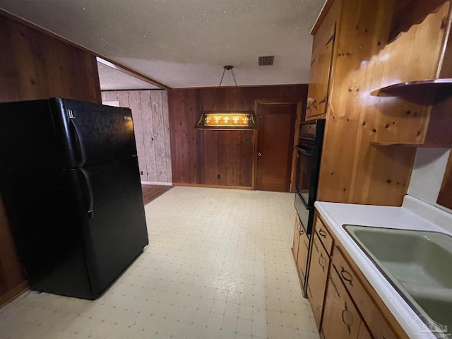 kitchen featuring visible vents, light floors, wood walls, freestanding refrigerator, and a sink