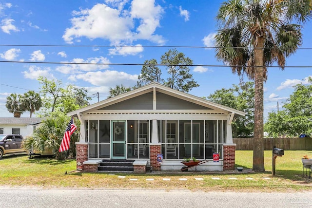 view of front of home featuring fence, entry steps, a sunroom, and a front lawn