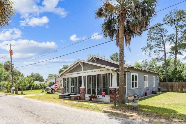 bungalow-style house with fence, a sunroom, and a front lawn