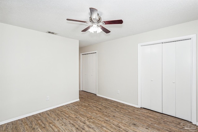 unfurnished bedroom with ceiling fan, wood-type flooring, a textured ceiling, and multiple closets