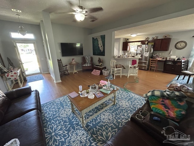 living room featuring ceiling fan, light wood-type flooring, a textured ceiling, and visible vents