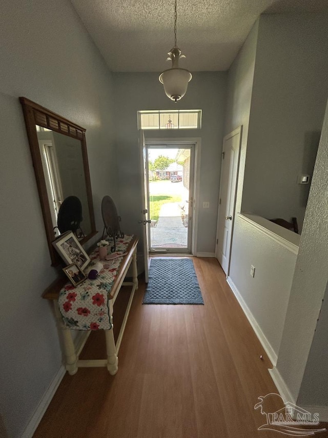 doorway featuring baseboards, light wood finished floors, and a textured ceiling