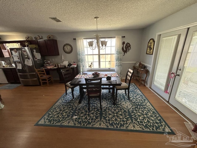 dining area with a textured ceiling, a chandelier, wood finished floors, and visible vents