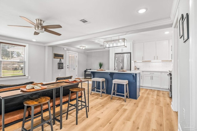 kitchen featuring crown molding, a center island with sink, stainless steel appliances, white cabinets, and a kitchen bar