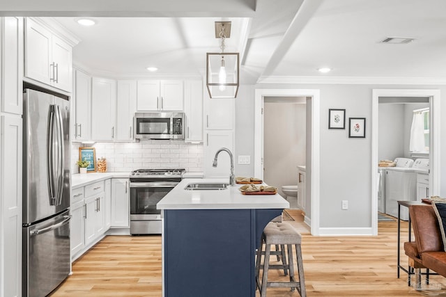 kitchen with a kitchen island with sink, white cabinets, light hardwood / wood-style floors, appliances with stainless steel finishes, and washing machine and clothes dryer