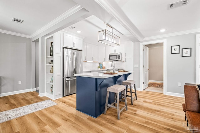 kitchen with pendant lighting, white cabinets, appliances with stainless steel finishes, a center island, and light wood-type flooring