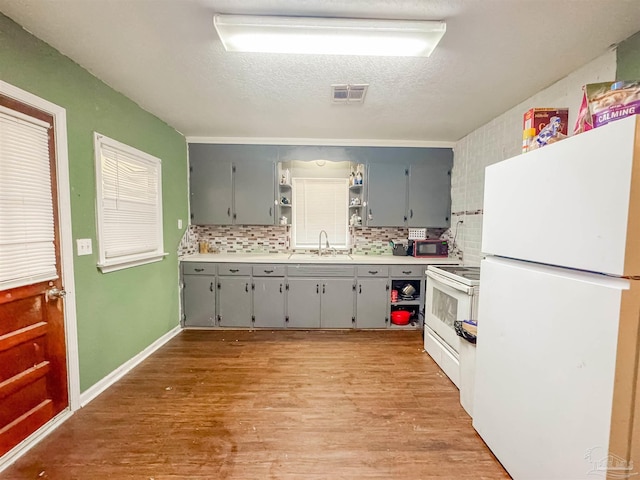 kitchen with sink, light wood-type flooring, gray cabinets, white appliances, and decorative backsplash