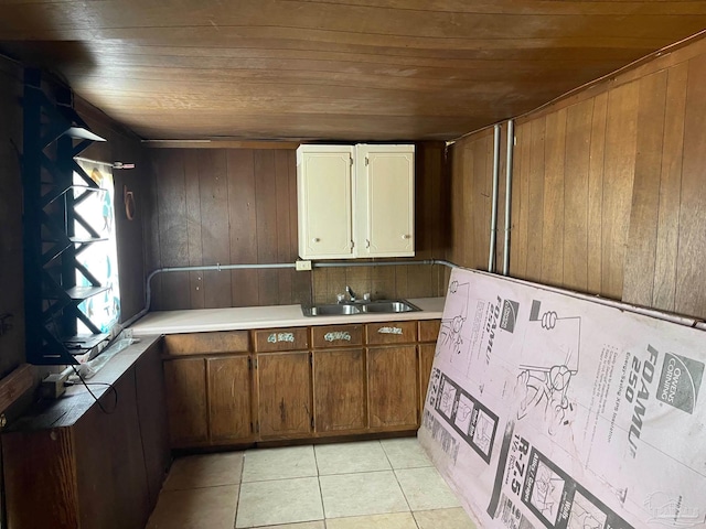 kitchen with light tile patterned floors, light countertops, wood ceiling, a sink, and wood walls