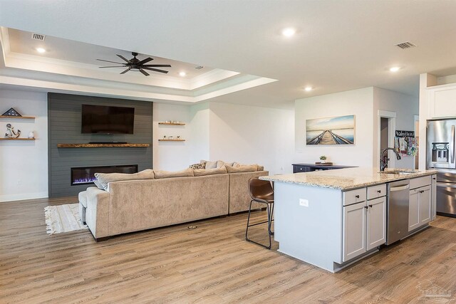 3564 Sailfish Dr, Gulf Breeze, FL 32563 - kitchen featuring stainless steel appliances, open floor plan, light wood finished floors, a raised ceiling, and a kitchen island with sink