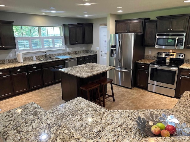 kitchen with appliances with stainless steel finishes, a sink, light stone countertops, recessed lighting, and a kitchen bar