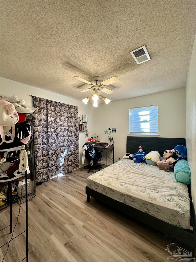 bedroom with light hardwood / wood-style flooring, ceiling fan, and a textured ceiling