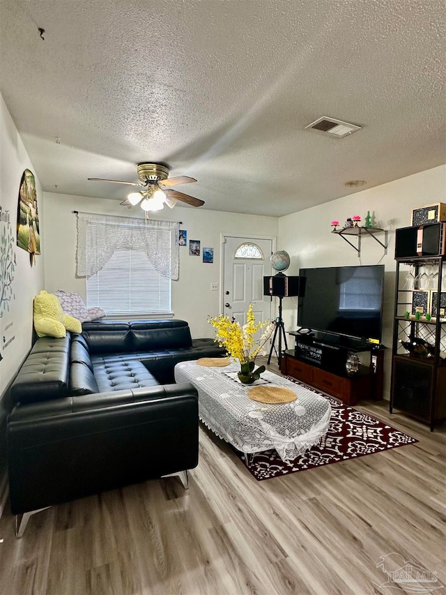 living room featuring ceiling fan, a textured ceiling, and wood-type flooring