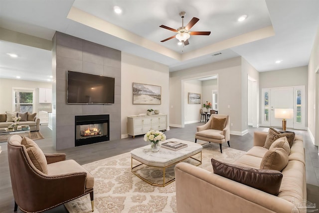 living room with a tray ceiling, a tile fireplace, and light hardwood / wood-style floors