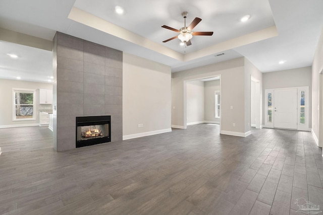 unfurnished living room with a fireplace, dark hardwood / wood-style floors, ceiling fan, and a raised ceiling