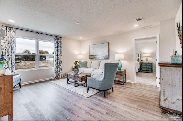 living room featuring visible vents, baseboards, wood finished floors, and a textured ceiling