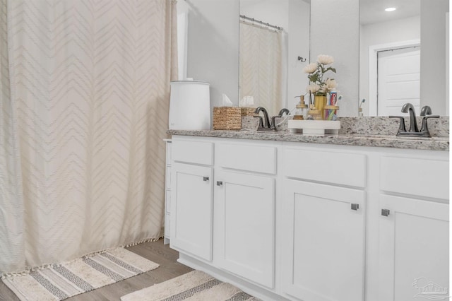 bathroom with a shower with shower curtain, double vanity, a sink, and wood finished floors