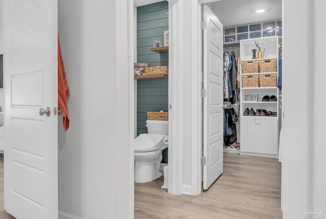 bathroom featuring toilet, wood finished floors, baseboards, and a walk in closet