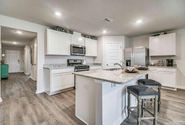 kitchen featuring a kitchen bar, a kitchen island with sink, light wood-style flooring, and stainless steel appliances