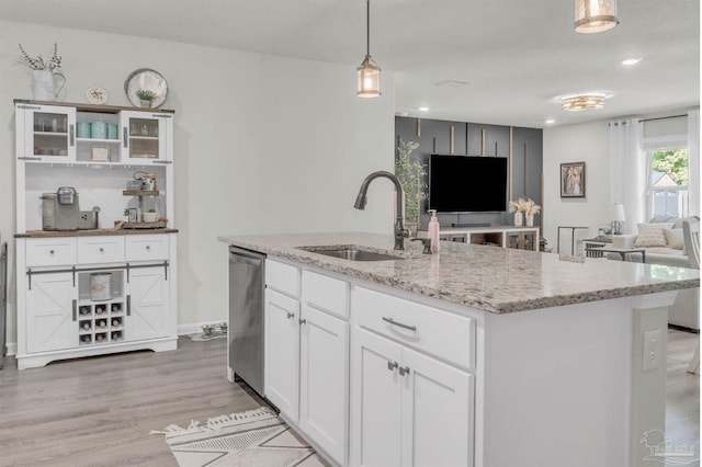 kitchen with light stone counters, open floor plan, light wood-style floors, stainless steel dishwasher, and a sink