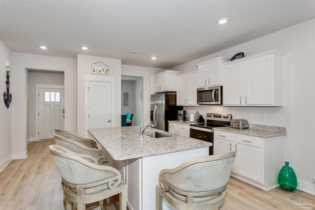 kitchen featuring stainless steel appliances, a sink, white cabinetry, an island with sink, and a kitchen bar