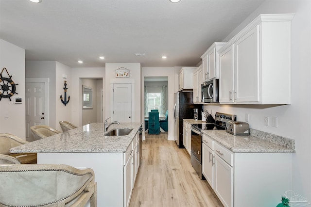 kitchen featuring a center island with sink, a breakfast bar area, appliances with stainless steel finishes, white cabinets, and a sink