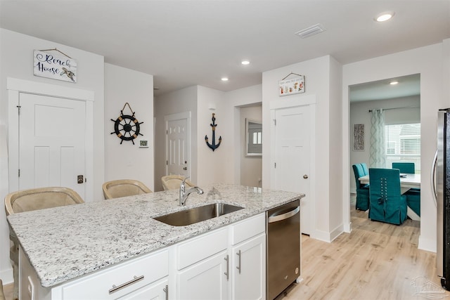 kitchen with light stone counters, a sink, white cabinetry, stainless steel dishwasher, and a center island with sink