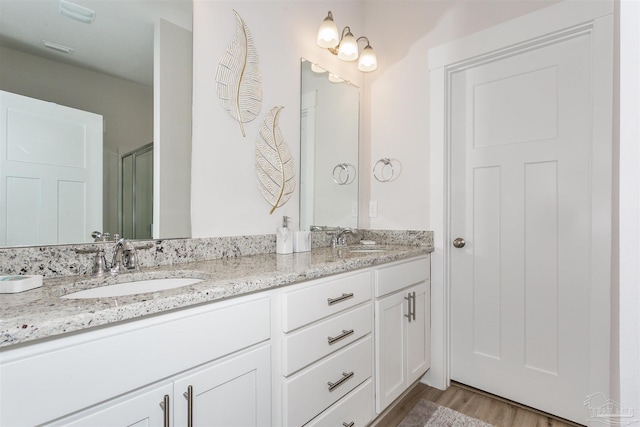 bathroom with an enclosed shower, double vanity, wood finished floors, and a sink