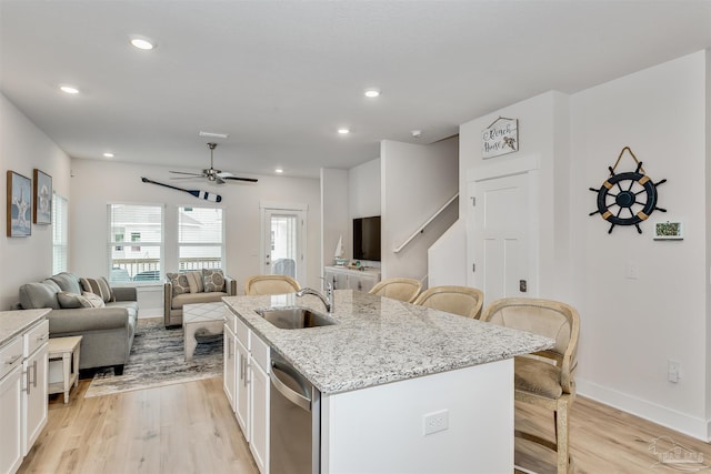 kitchen with a kitchen island with sink, a breakfast bar, white cabinets, open floor plan, and dishwasher