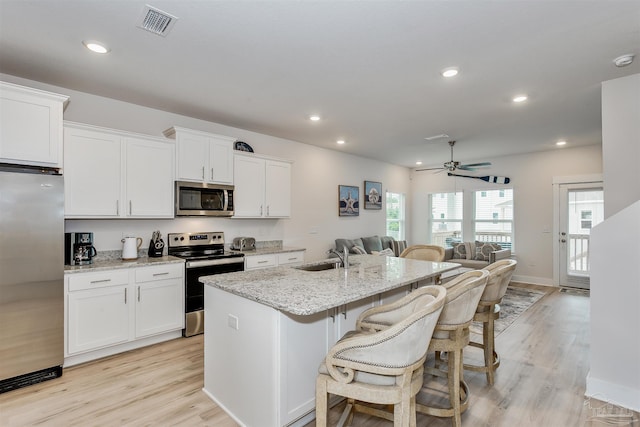 kitchen with an island with sink, appliances with stainless steel finishes, white cabinets, and light stone counters