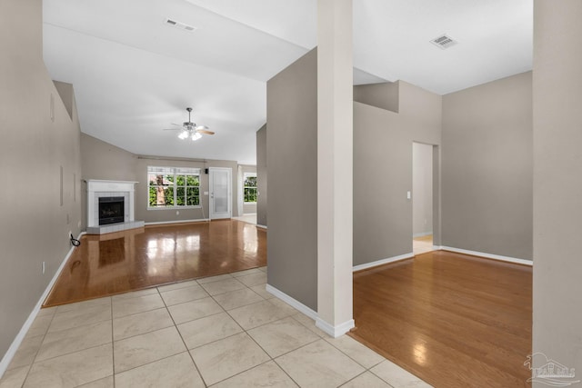 unfurnished living room with a ceiling fan, vaulted ceiling, visible vents, light wood finished floors, and baseboards
