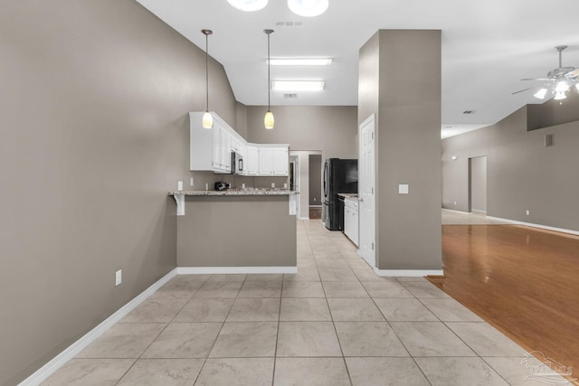 kitchen with a peninsula, a high ceiling, freestanding refrigerator, white cabinets, and ceiling fan